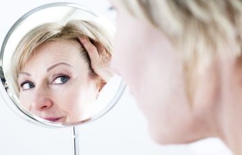Mature woman watching her eye area in a mirror.